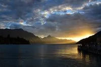 Dramatic sunset over Lake Wakatipu in Queenstown, highlighting mountain silhouettes and vibrant skies